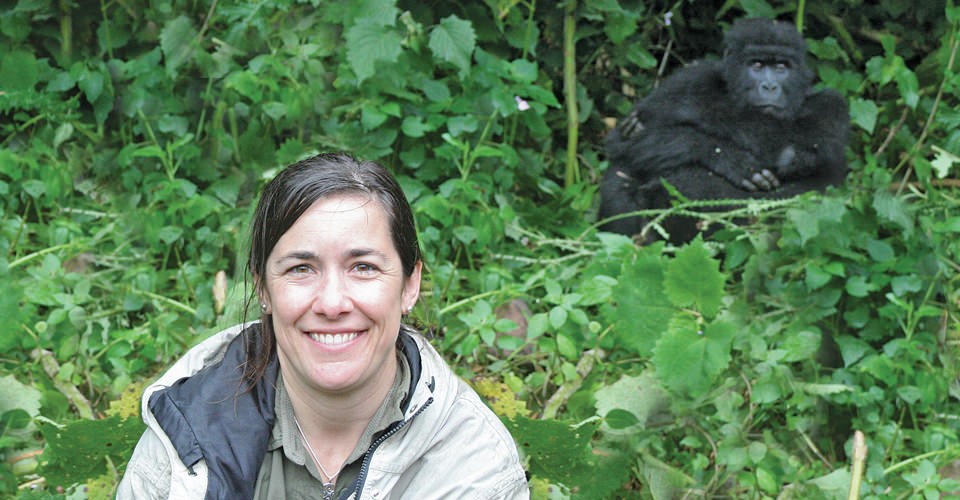 a woman sits in the brush with a large gorilla behind her