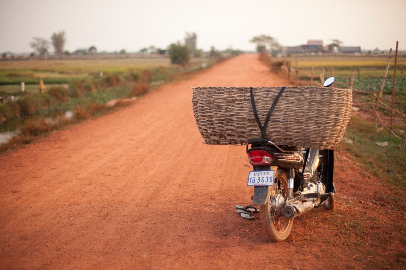 a motorbike with a basket sits on a dirt road in the countryside of cambodia