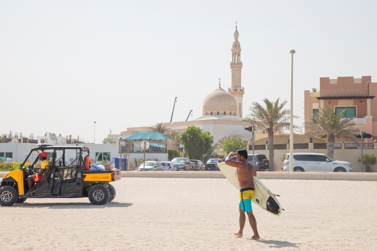 a surfer walks along the sand in Dubai