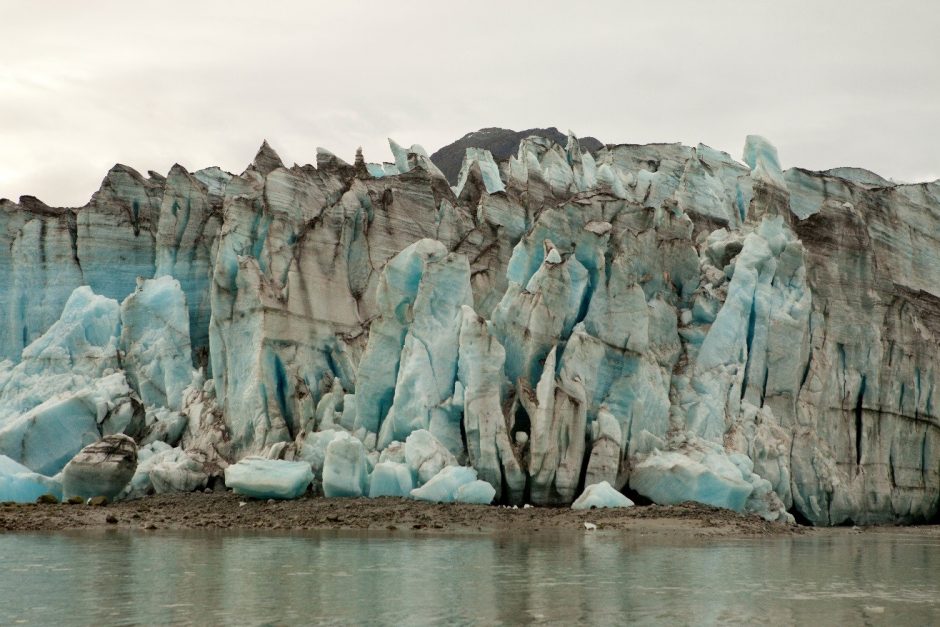 a jagged glacier comes closely to the water's edge in Alaska