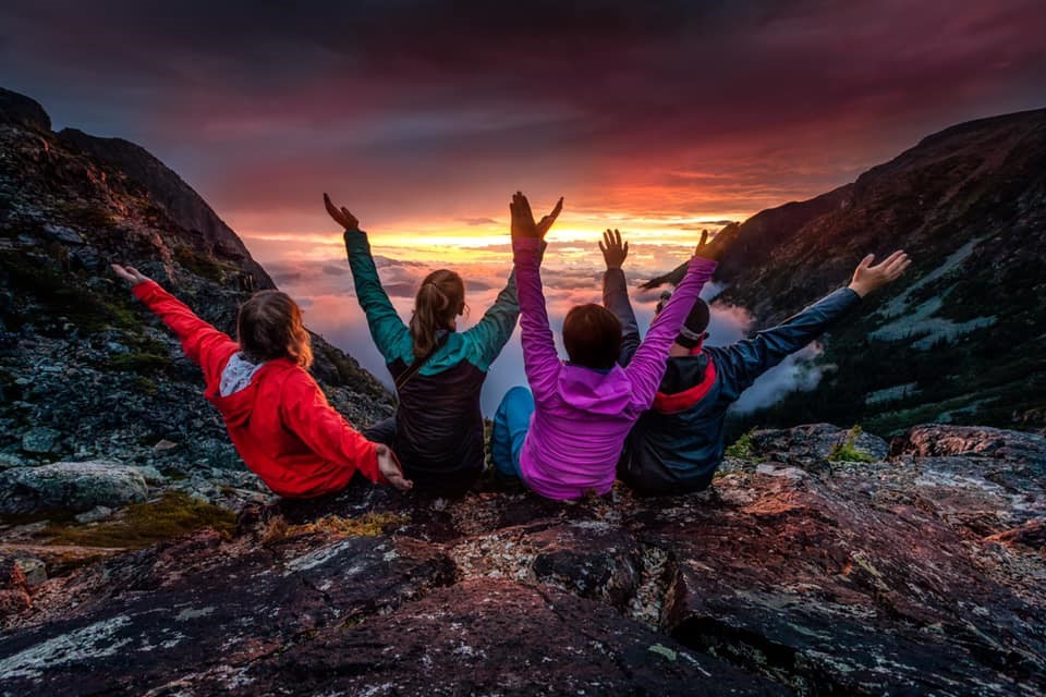 four friends show exuberance as the sun sets in the distance