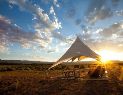 a canvas tent sits in the desert with sun setting