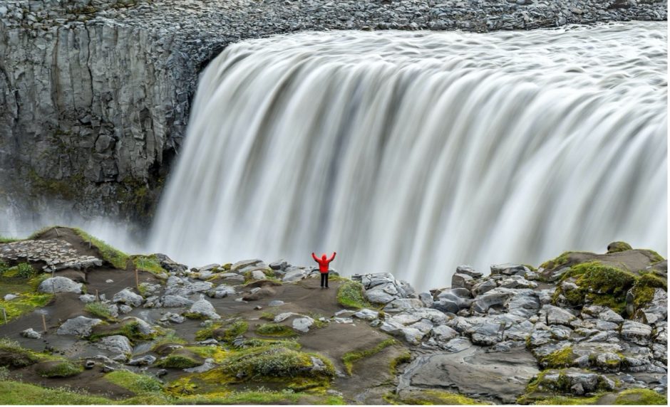 an adventurer stands in front of an amazing silky waterfall in iceland