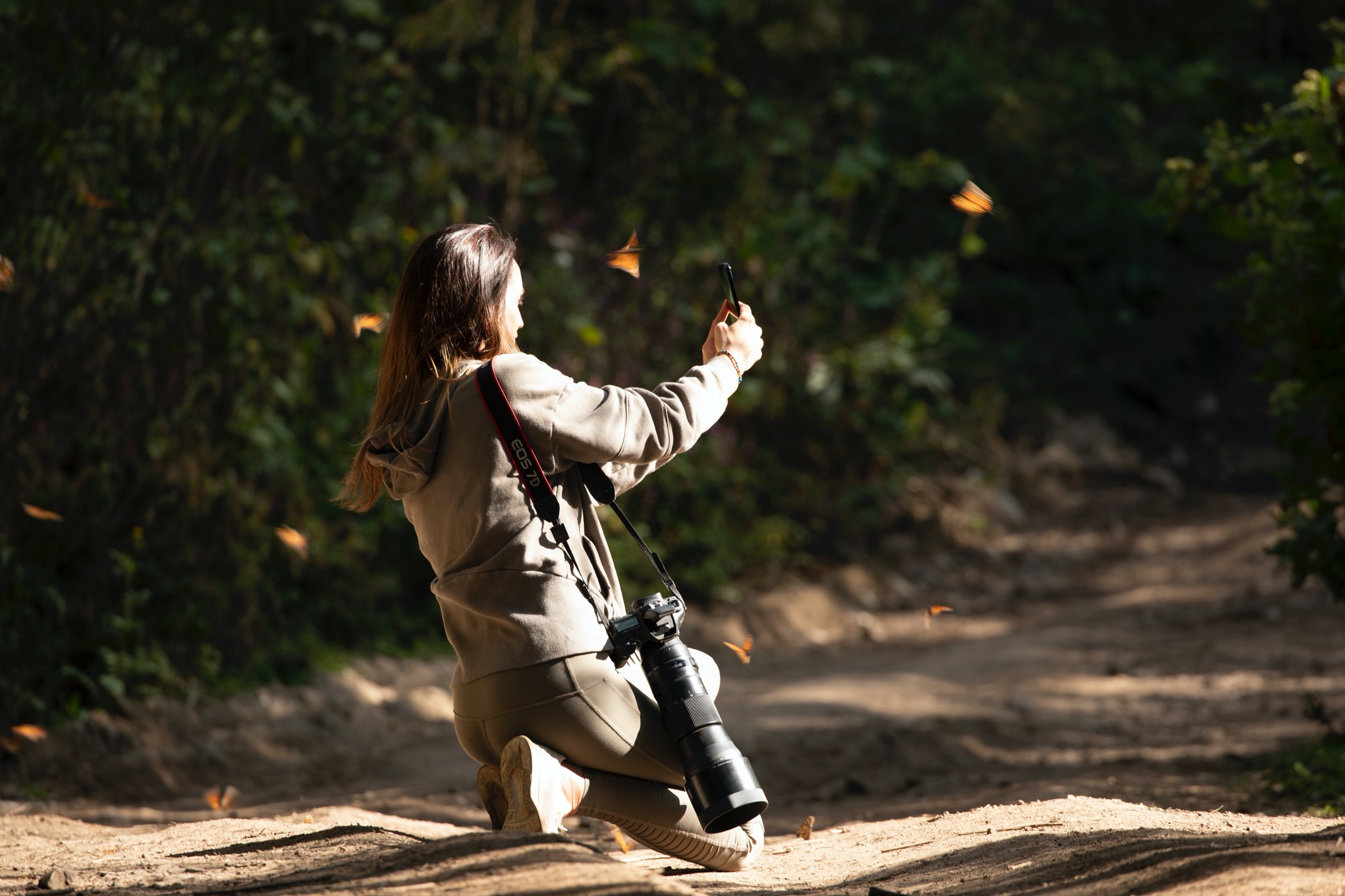 a woman takes a photo while surrounded by monarch butterflies