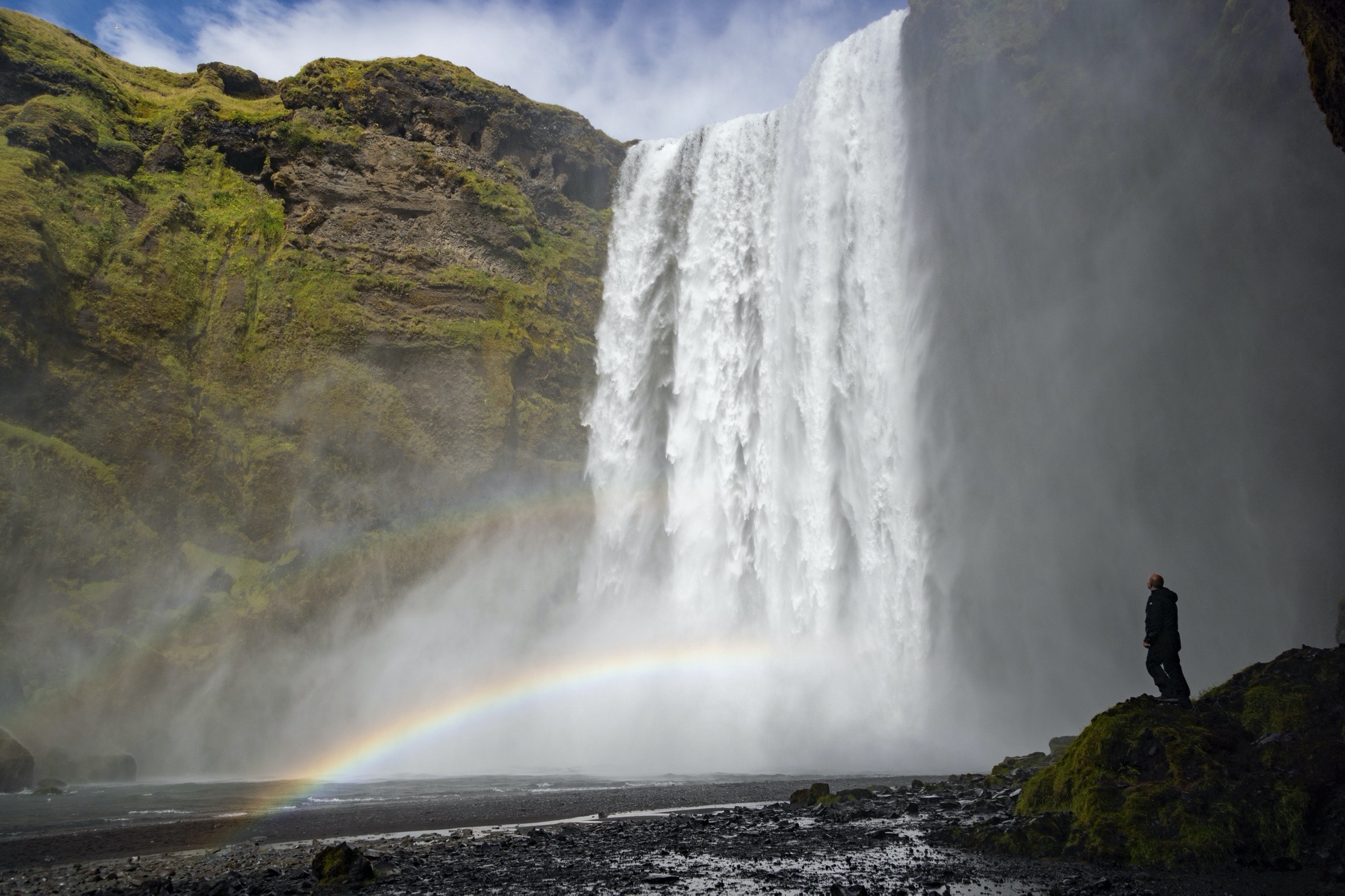 Skogafoss waterfall towers over a hiker