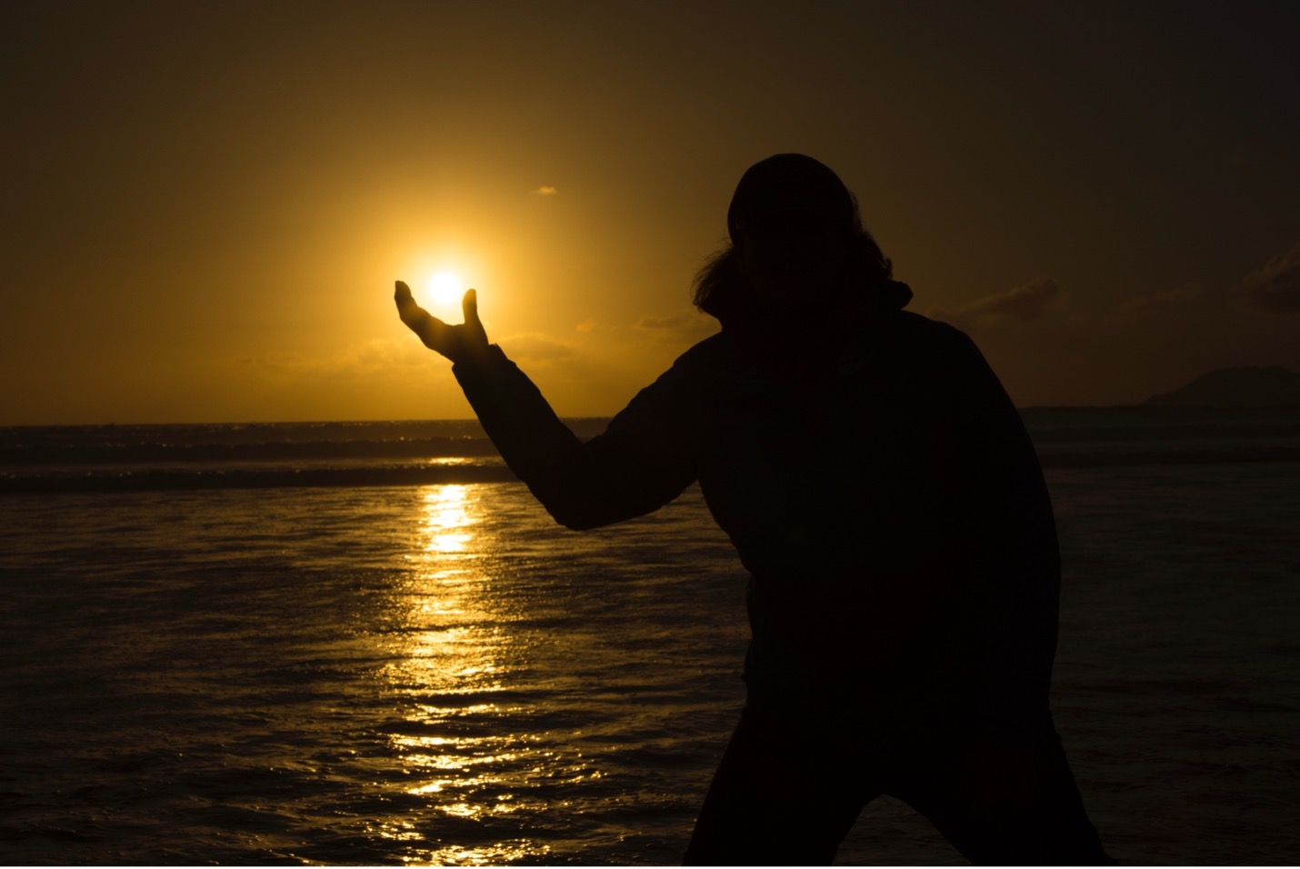 a woman cups the sun in her hands as it descends for the night