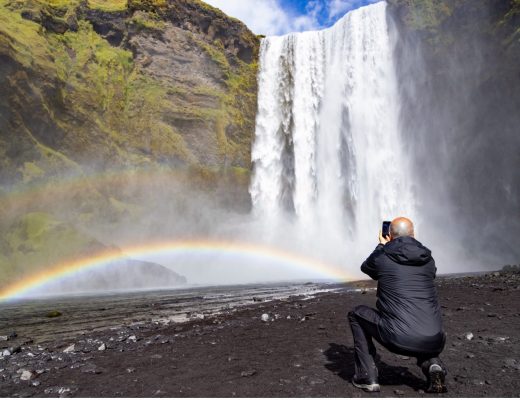 a man crouches to photograph a waterfall in iceland