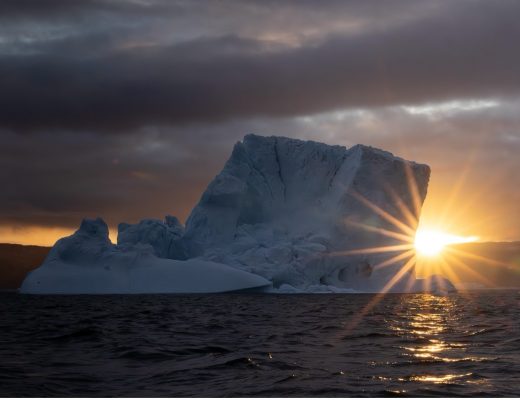 a large iceberg with sunburst on the horizon