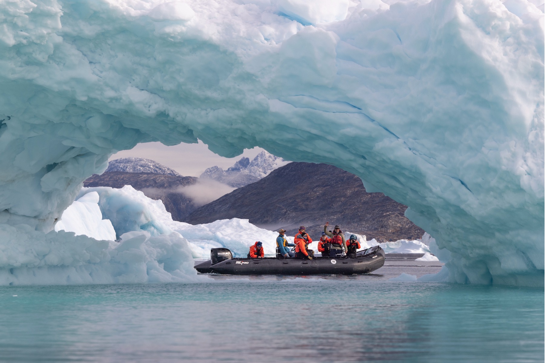 a boat sits perfectly under an ice arch in greenland