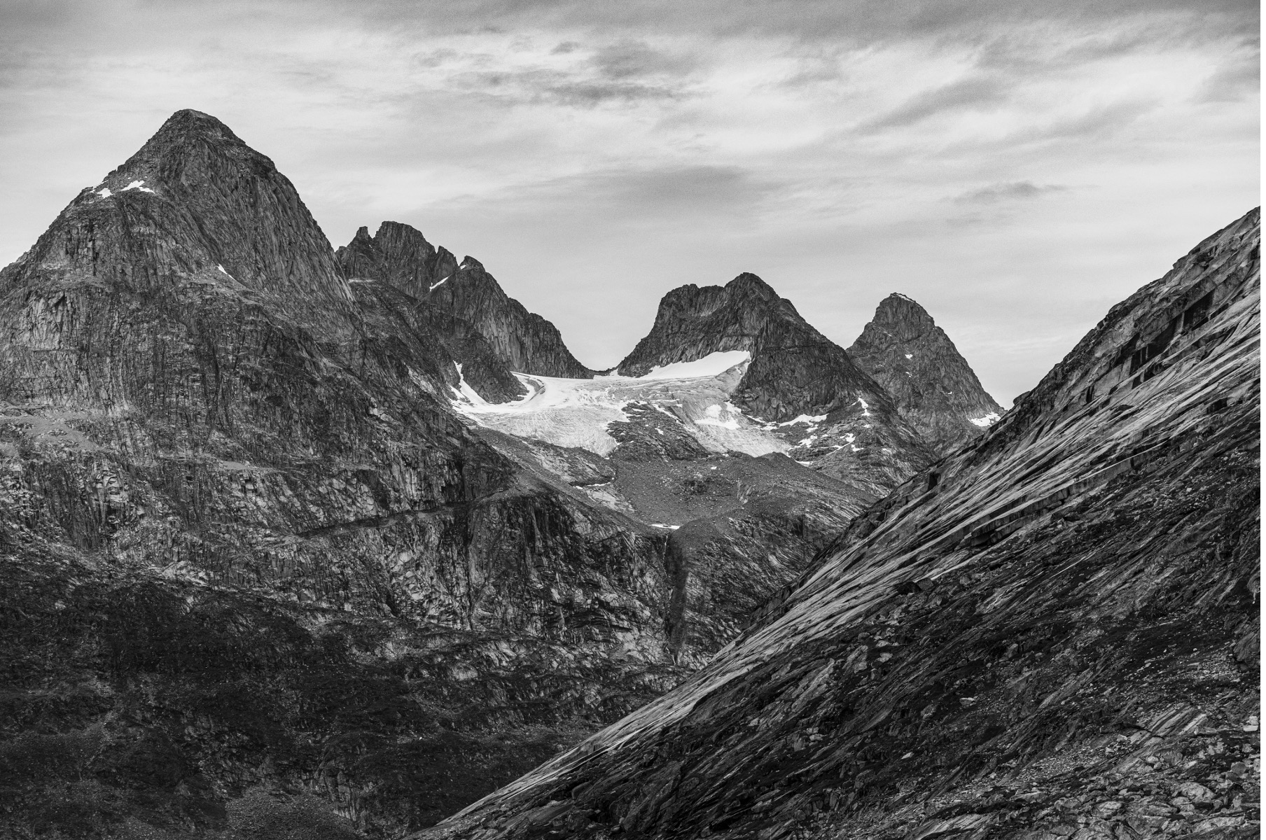 a glacier contrasts dark mountain peaks in greenland